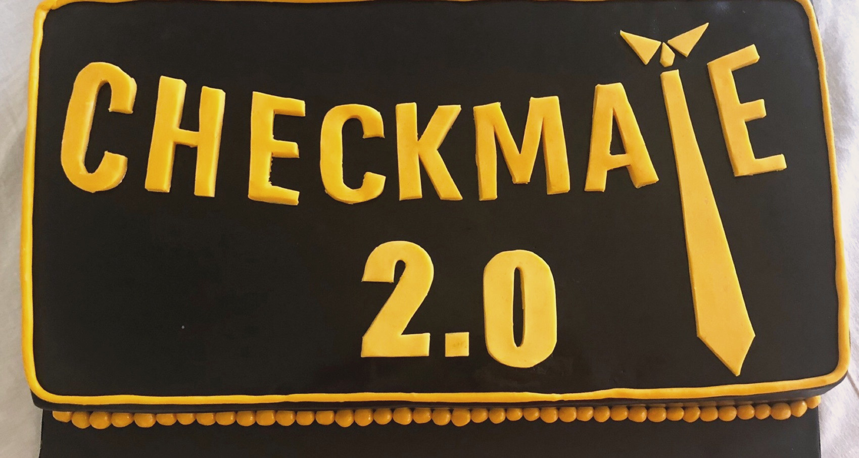 Black cake with the Checkmate 2.0 logo in yellow fondant